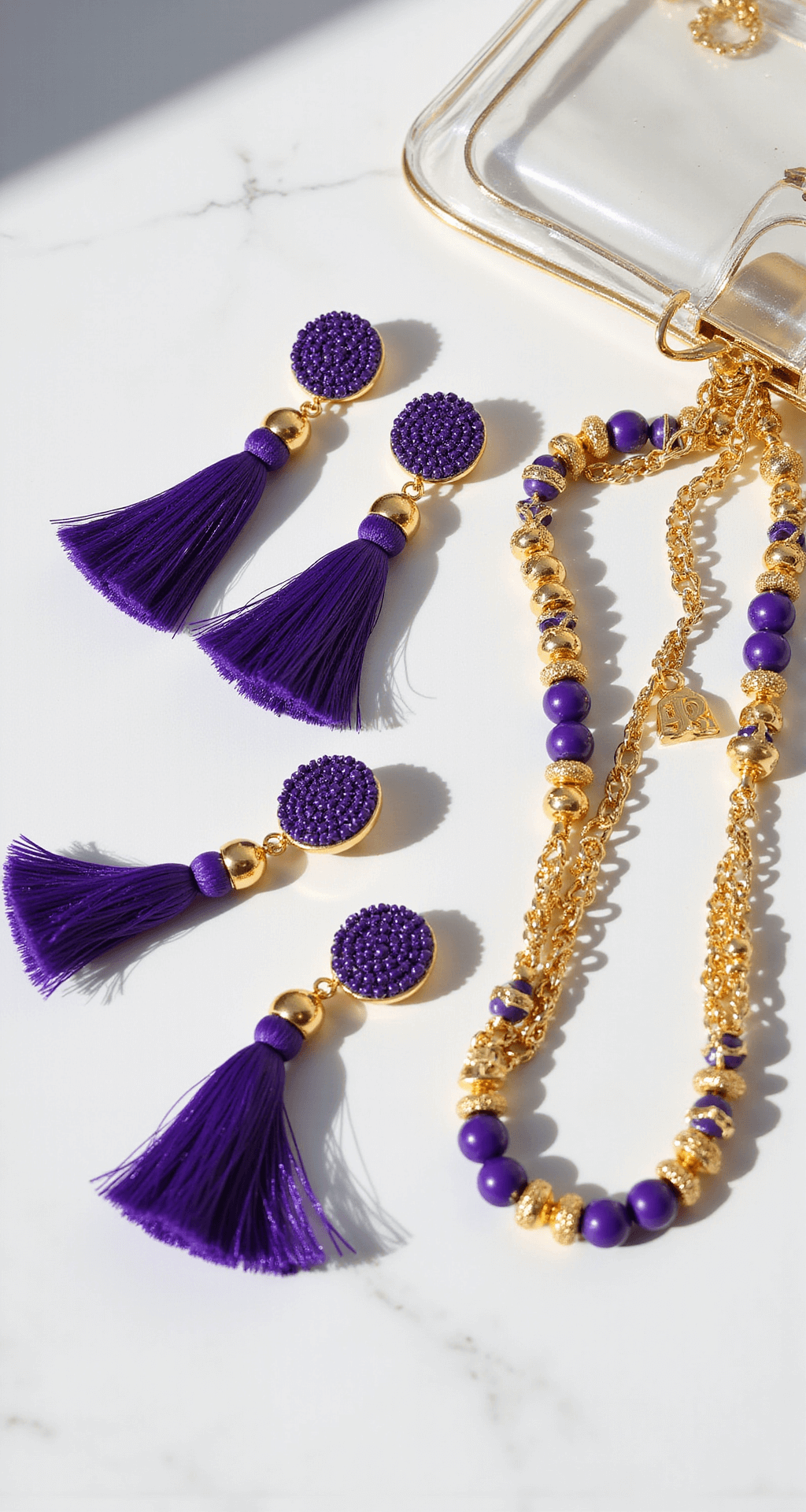 The Ultimate LSU Game Day Style Close-up of gameday accessories including purple tassel earrings, layered gold necklaces, purple and gold beaded bracelets, and a clear stadium bag with charm accents, arranged on a marble surface against a white backdrop.