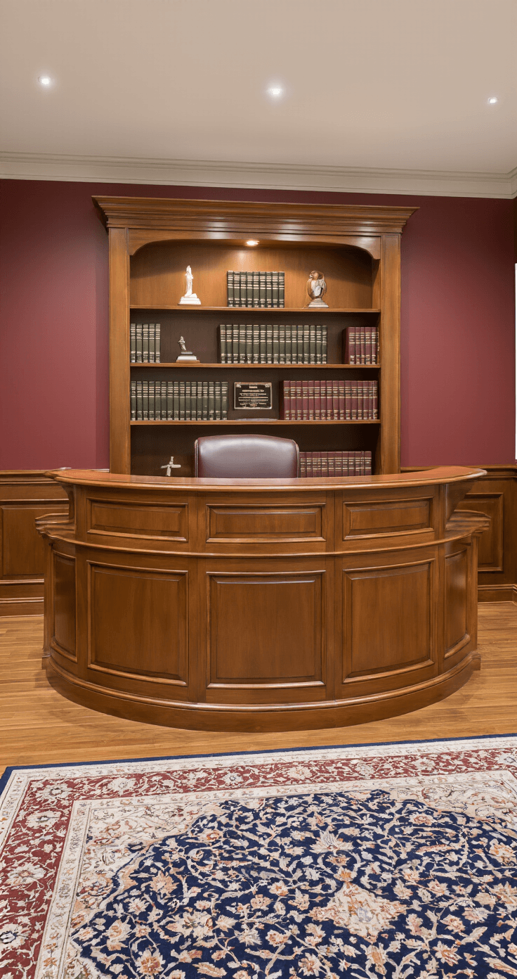 An ADA-compliant curved reception desk in mahogany with glass panels in a law firm entrance, featuring soft lighting, burgundy walls, and rich textures, highlighting accessibility and craftsmanship.